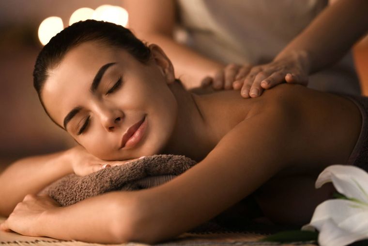 Person receiving a back massage while lying face down with eyes closed in a warmly lit spa setting