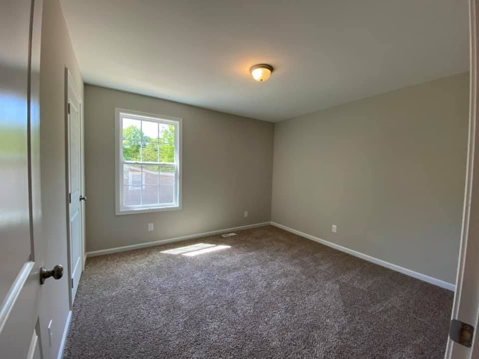 Empty beige bedroom with carpet, window, and closet doors, viewed from the doorway.