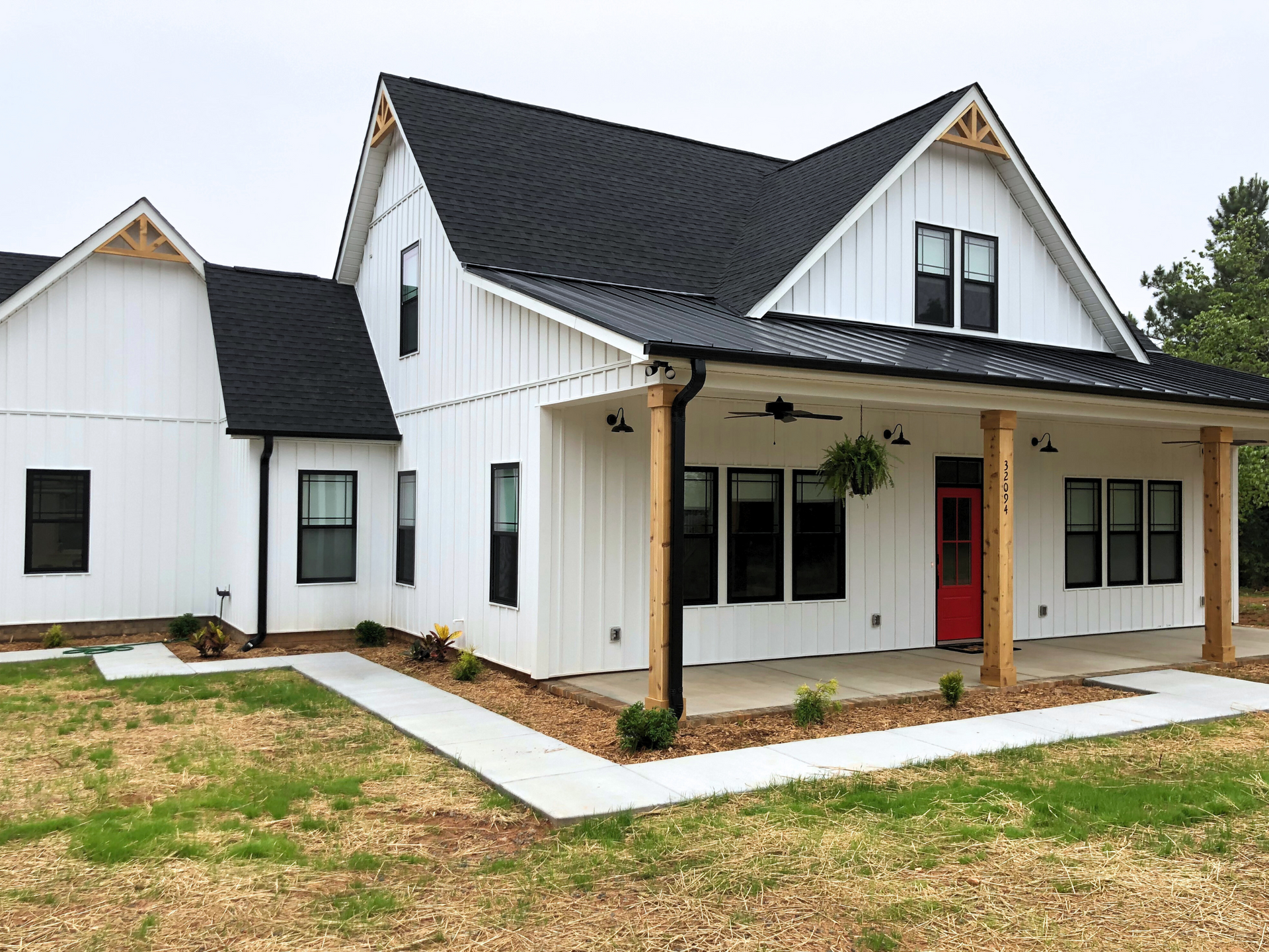 White farmhouse-style house with black roof, covered porch, and white trim on a grassy lot