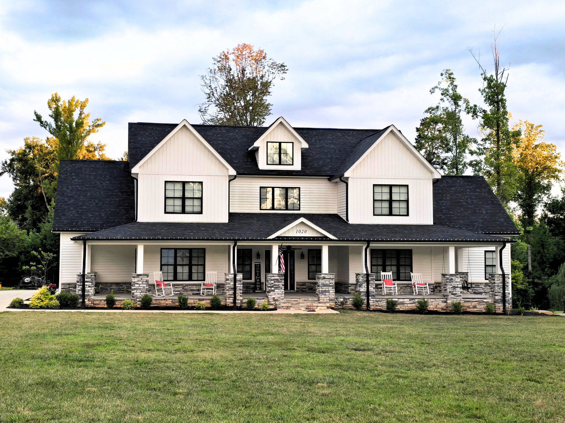 Large white farmhouse with black roof and wraparound porch on a grassy lawn