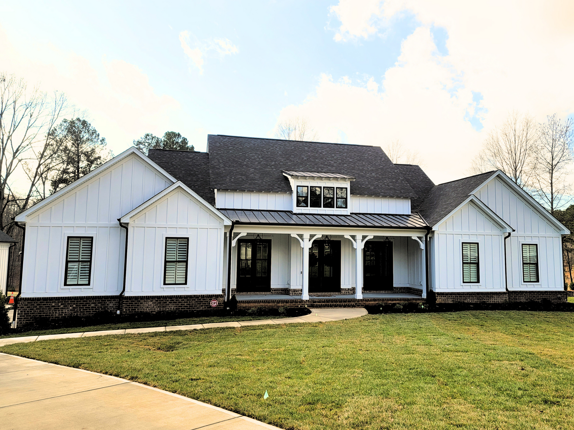 White house with black roof and front porch, set on a grassy lawn under a partly cloudy sky