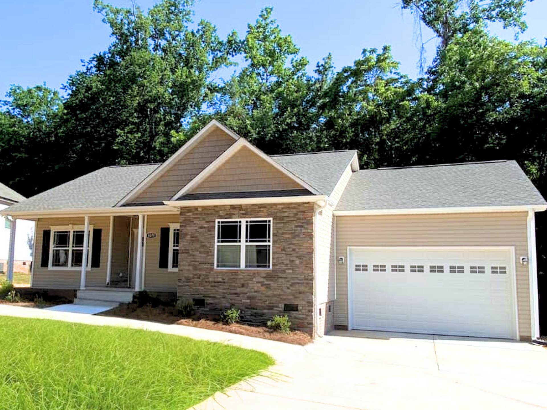 Suburban single-story beige house with attached garage, front porch, and green lawn under a clear sky