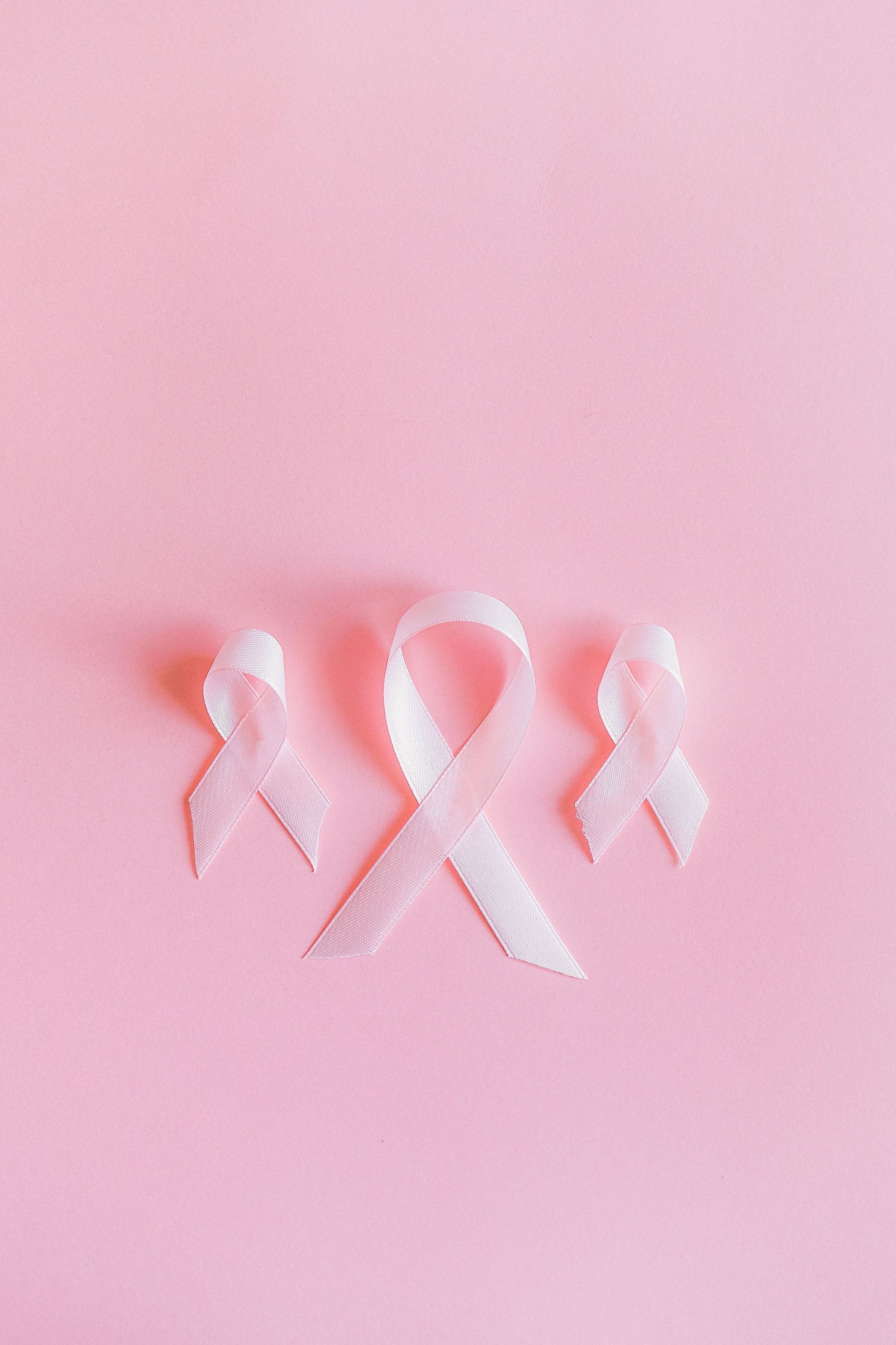 Pink breast cancer awareness ribbon with small angel wings on a pink background