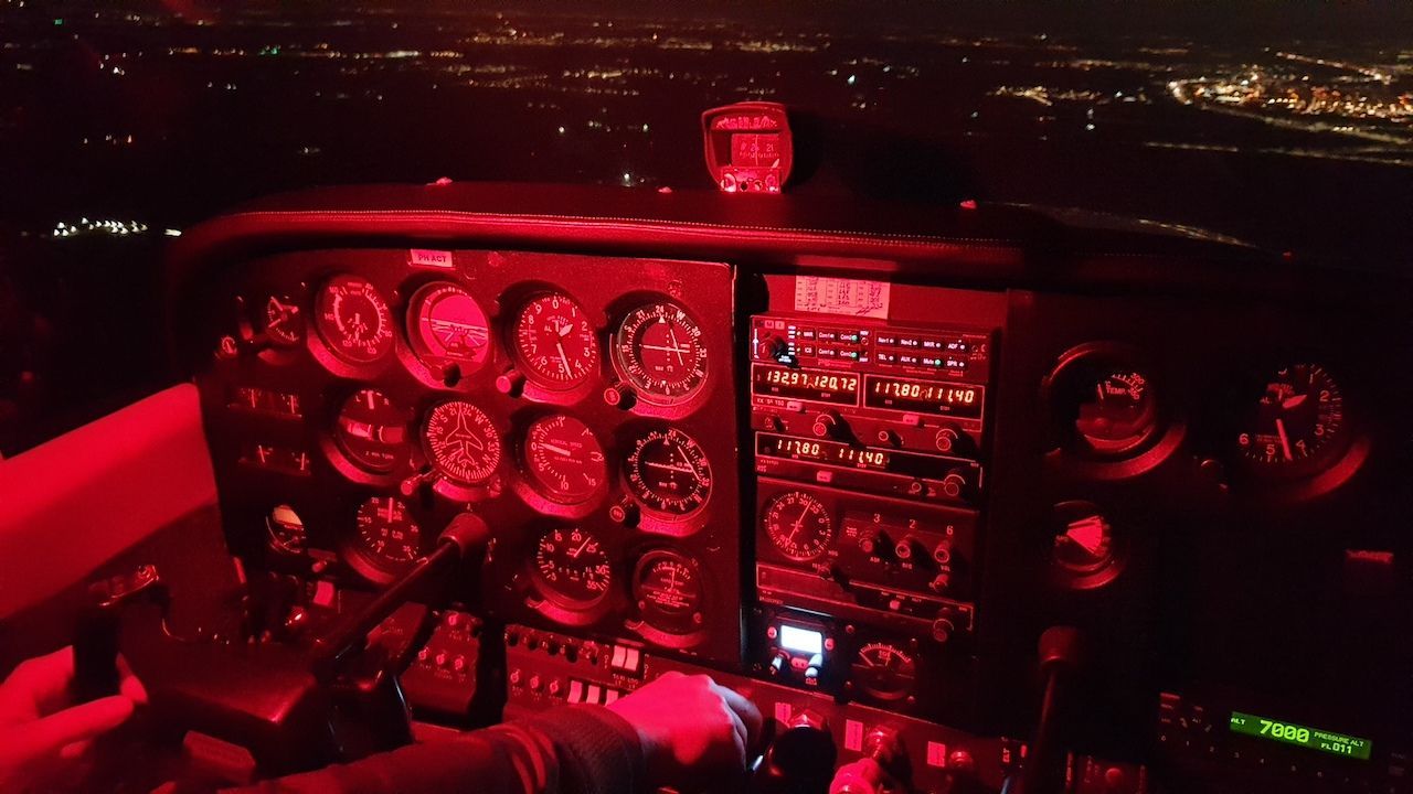 Rood verlicht dashboard van een vliegtuigcockpit met meerdere meters en bedieningselementen 's nachts