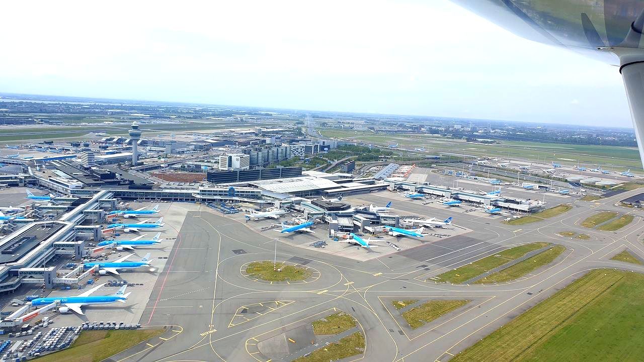 Luchthavenplatform met geparkeerde vliegtuigen en luchthavengebouwen onder een heldere hemel, gezien vanuit de lucht.