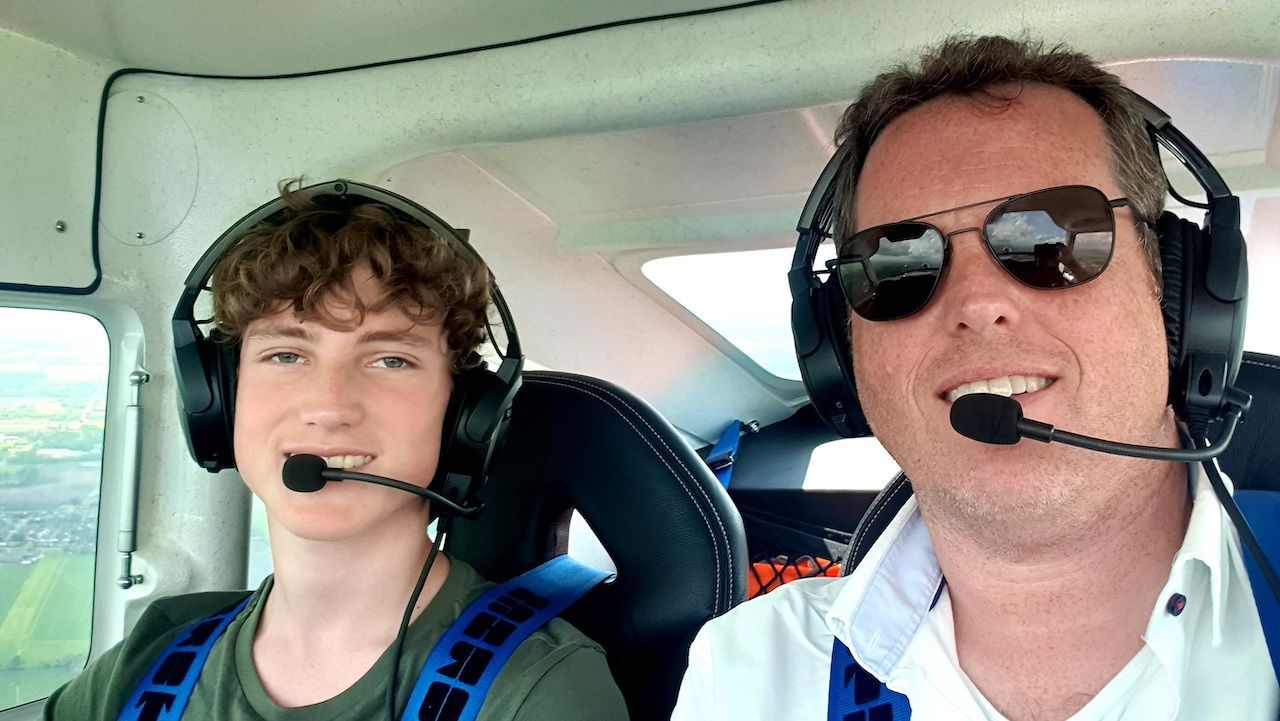 Twee lachende mensen met headsets op in de cockpit van een klein vliegtuig, waarvan er één het toestel bestuurt.