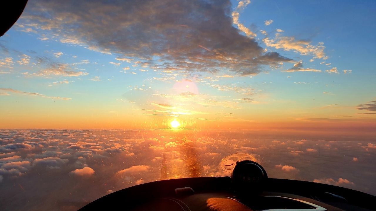 Zonsopgang boven de wolken met een gouden weerspiegeling, gezien vanuit een vliegtuigraam.