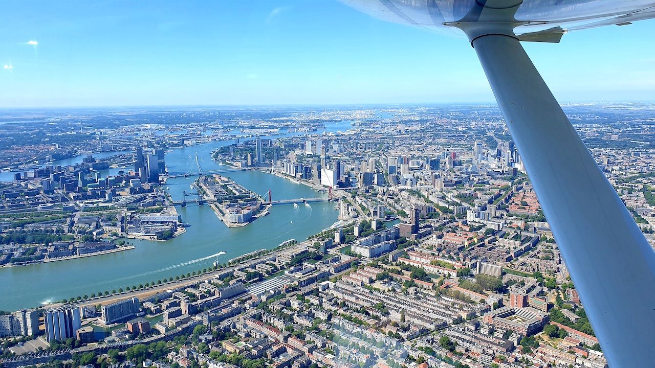 Luchtfoto van een kuststad met een rivier, bruggen en dichtbebouwde bebouwing, gezien vanuit een vliegtuigvleugel.