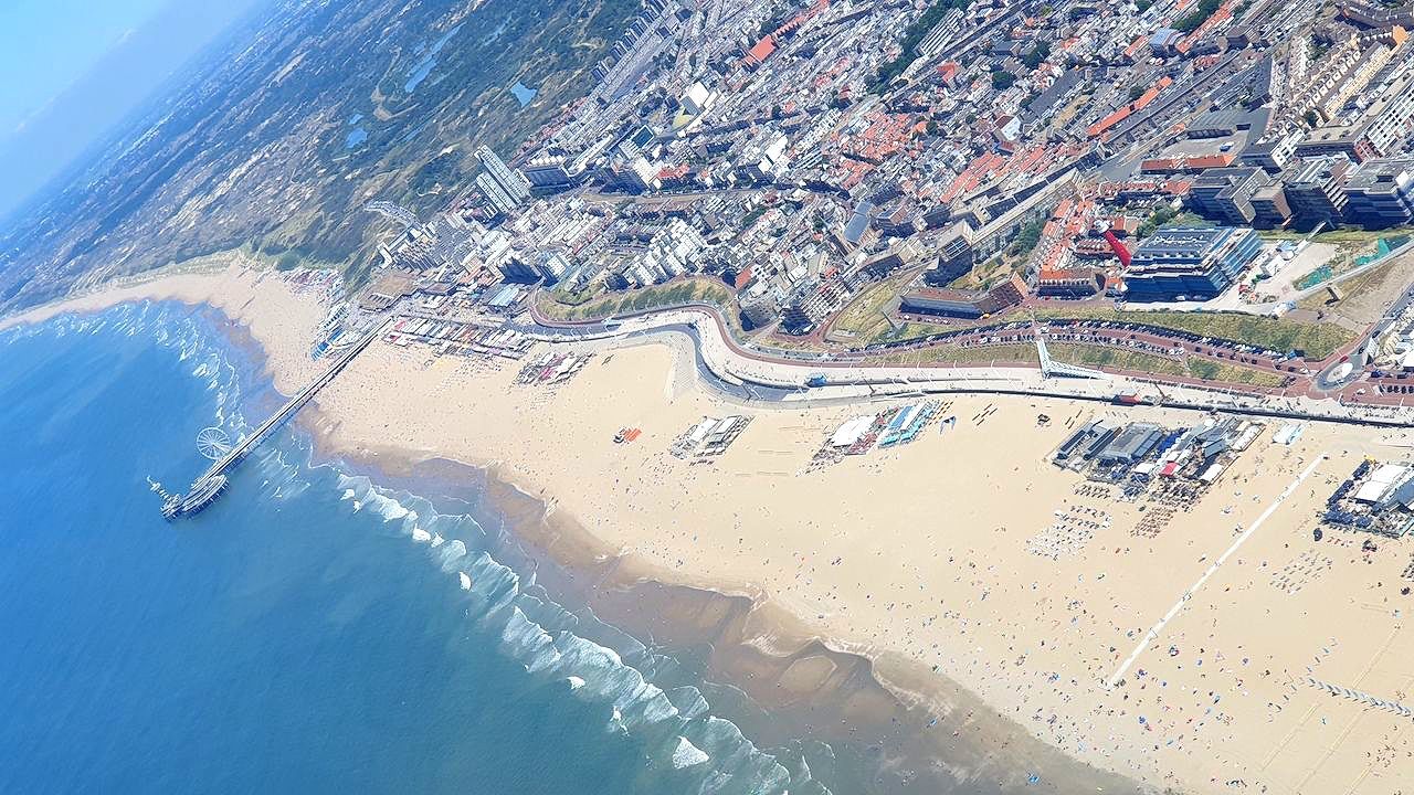 Luchtfoto van een druk zandstrand aan de blauwe oceaan en een kustplaats.