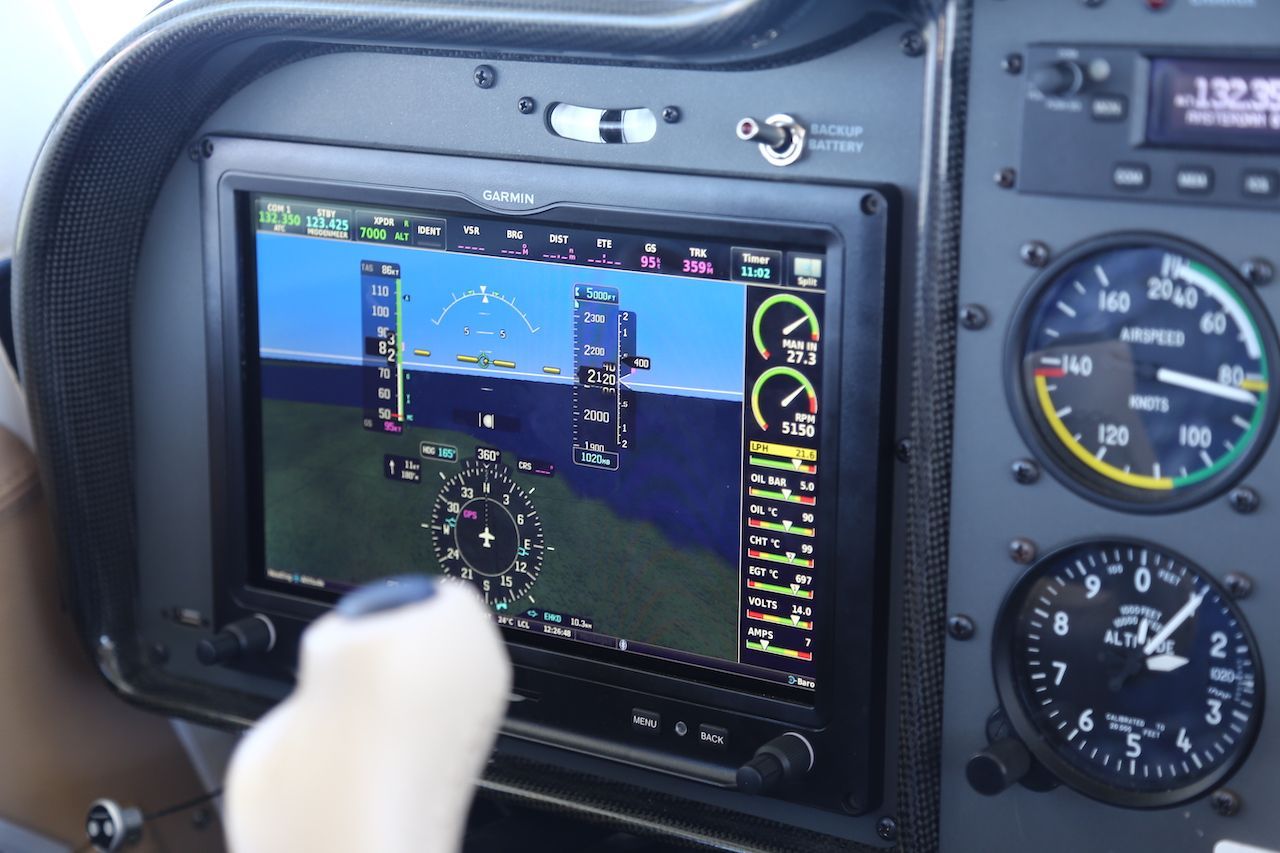 Vliegtuigcockpitdisplay met een vluchtsimulator en een witte joystick op de voorgrond.