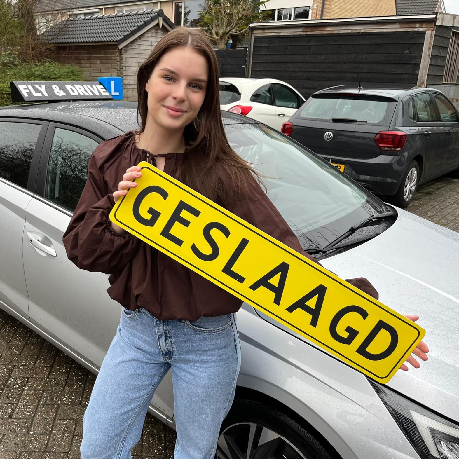 Vrouw staat naast een zilverkleurige auto, houdt een geel