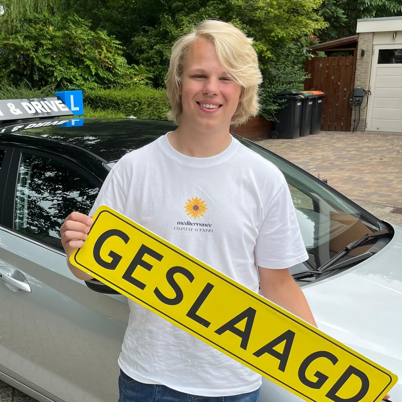 Een persoon lacht naast een auto en houdt een geel