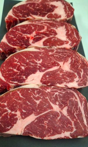 Four steaks are lined up on a black cutting board.