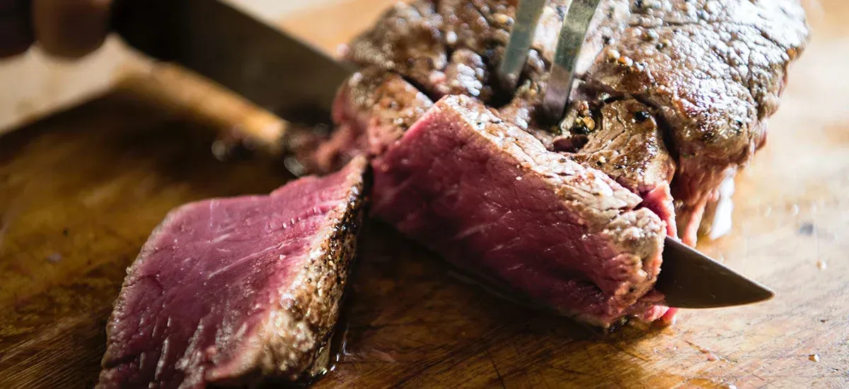 A person is cutting a large piece of meat on a cutting board.