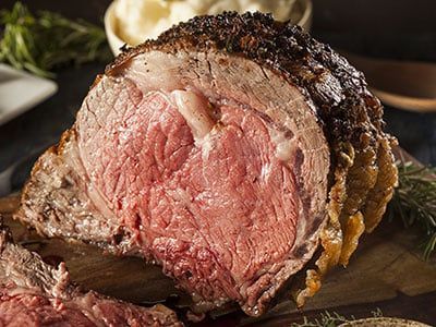A large piece of roast beef is sitting on a wooden cutting board.