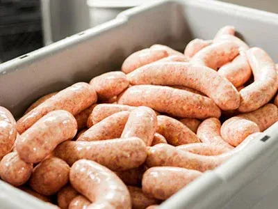 A plastic container filled with sausages in a kitchen.