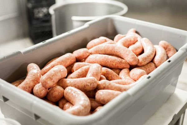 A plastic container filled with sausages is sitting on a counter.