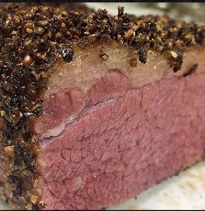 A close up of a piece of meat on a plate covered in pepper.