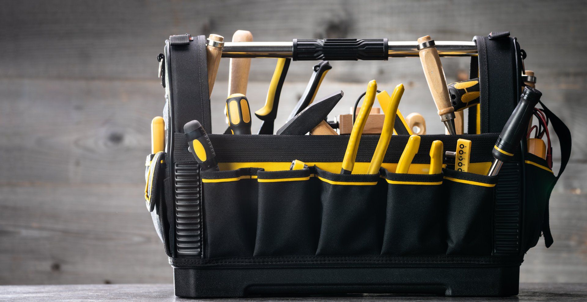 Black tool bag filled with yellow and black hand tools on a wooden surface