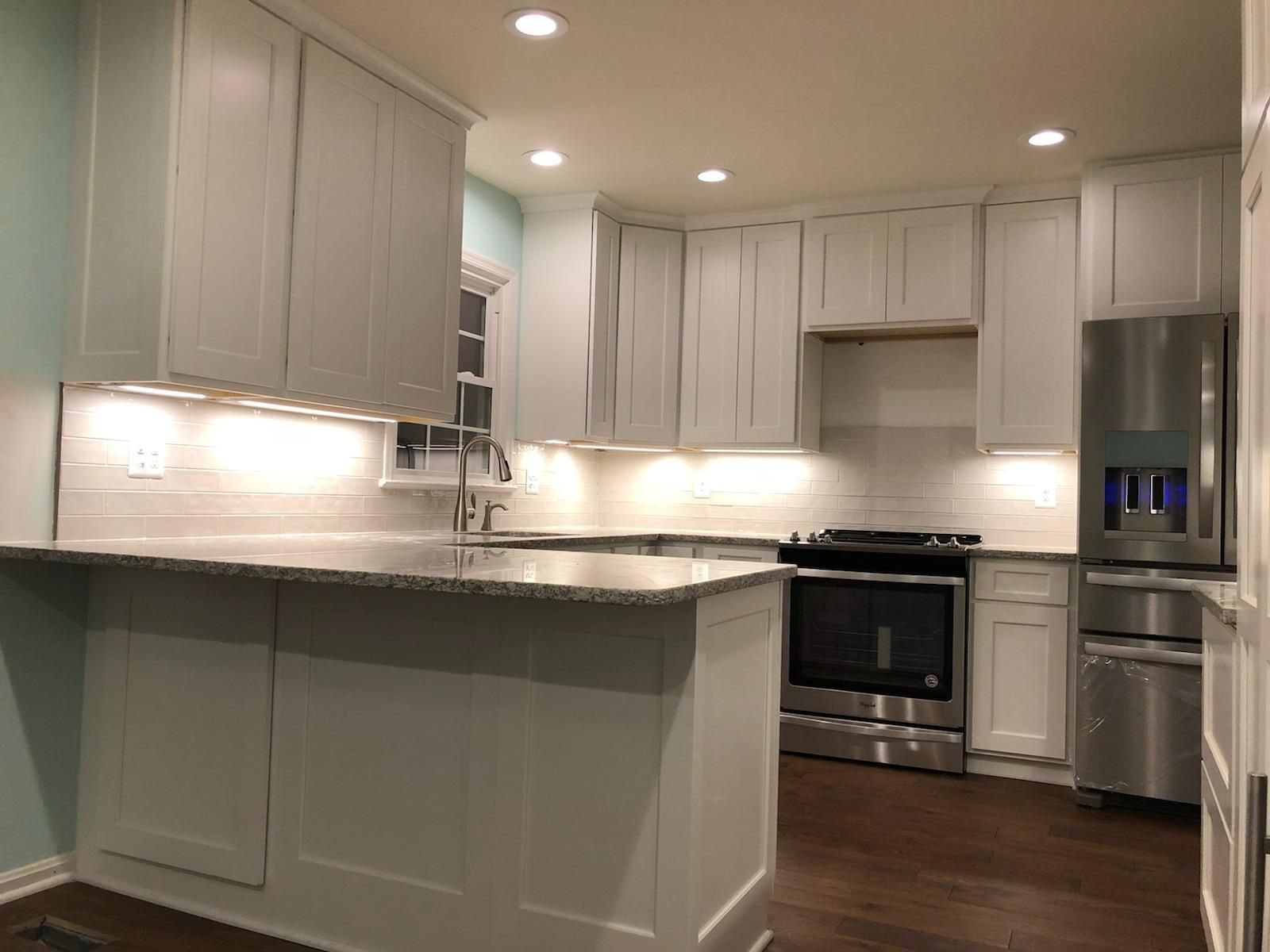 Modern white kitchen with granite island, recessed lighting, and stainless steel appliances