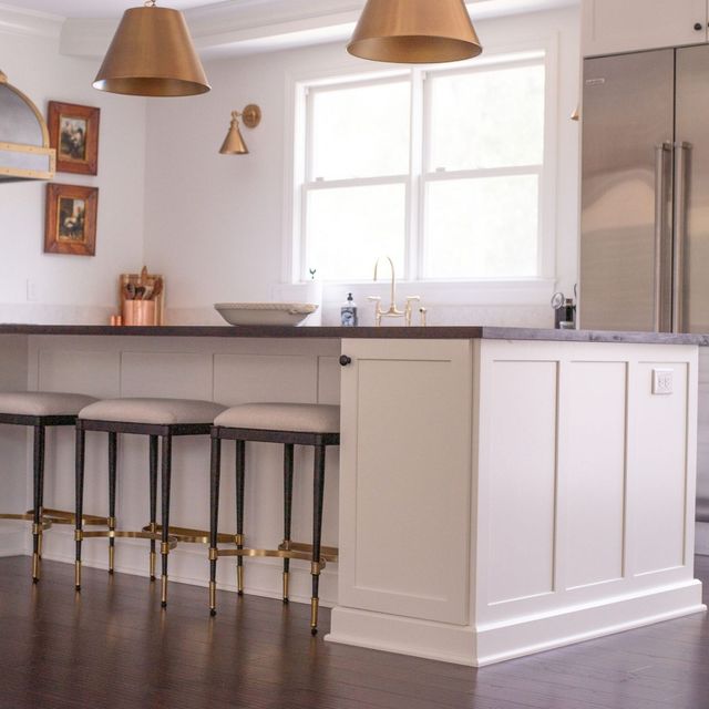 Modern kitchen with island, bar stools, pendant lights, and stainless steel refrigerator by a bright window