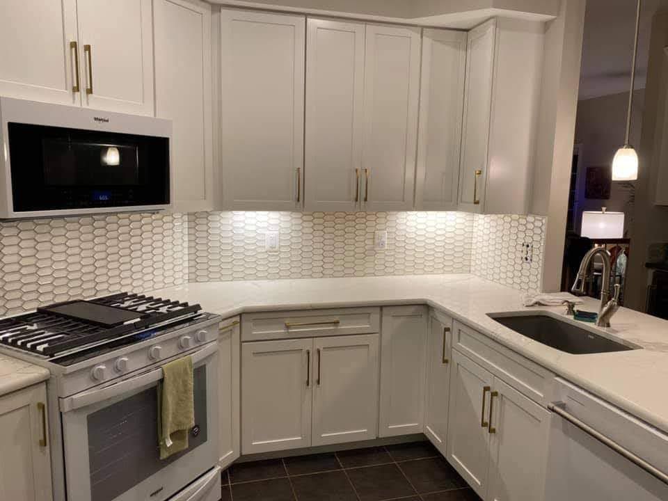 Modern white kitchen with tiled backsplash, stainless steel appliances, and L-shaped counter with sink
