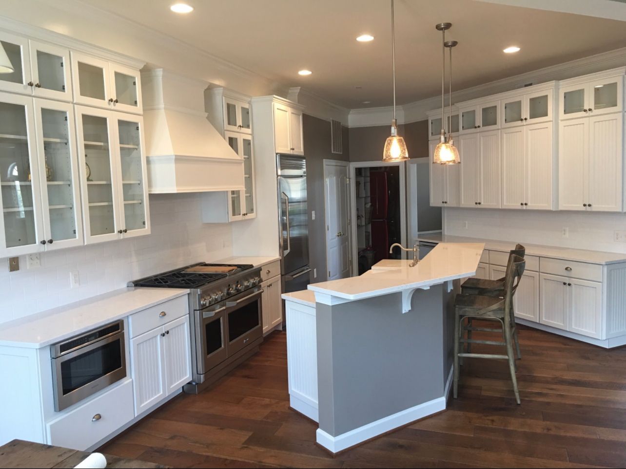Bright white kitchen with island, dark wood floors, stainless appliances, and pendant lights