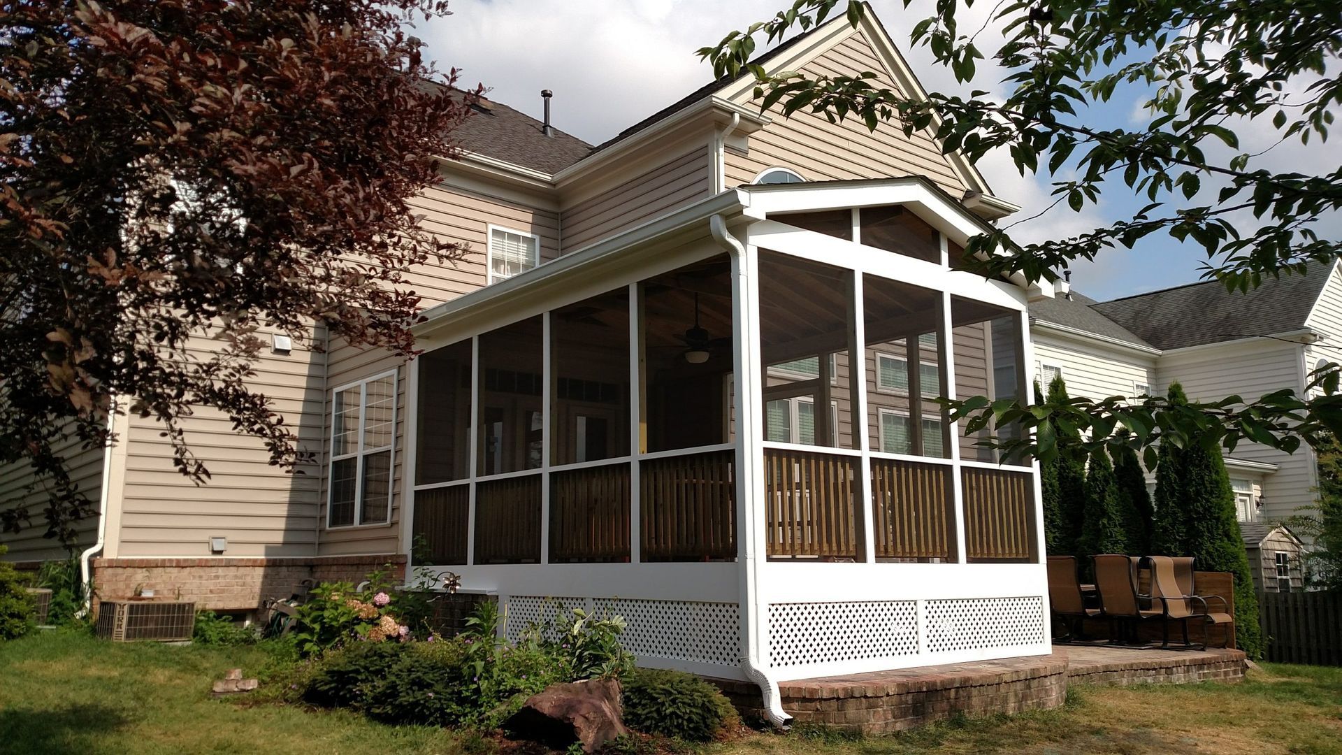 Screened porch on a beige house with white trim and a peaked roof in a leafy yard