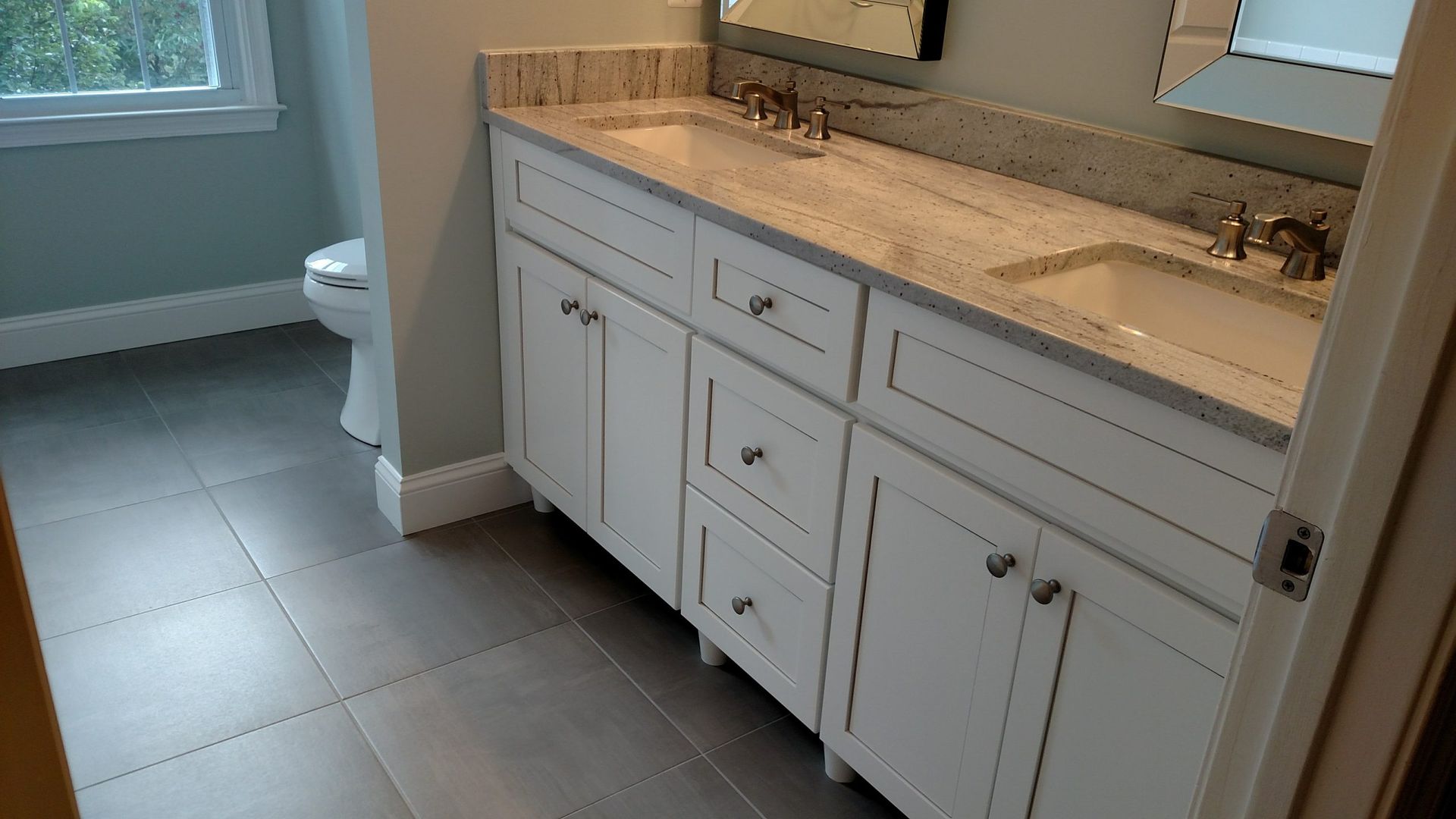 Bathroom vanity with white cabinets, beige countertop, mirror, and tiled floor near a toilet