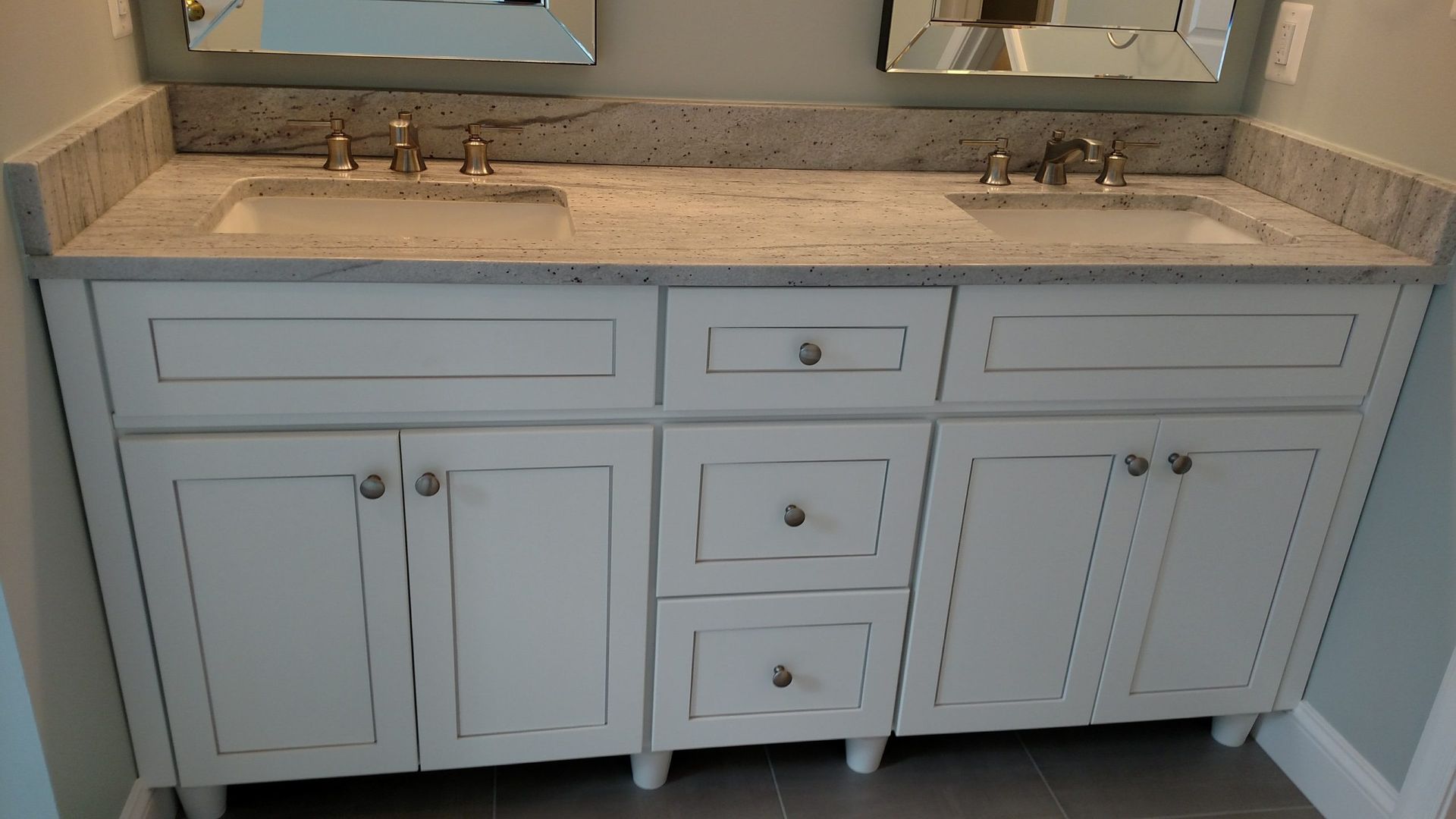 White bathroom vanity with marble countertop, double sinks, and mirrored backsplash