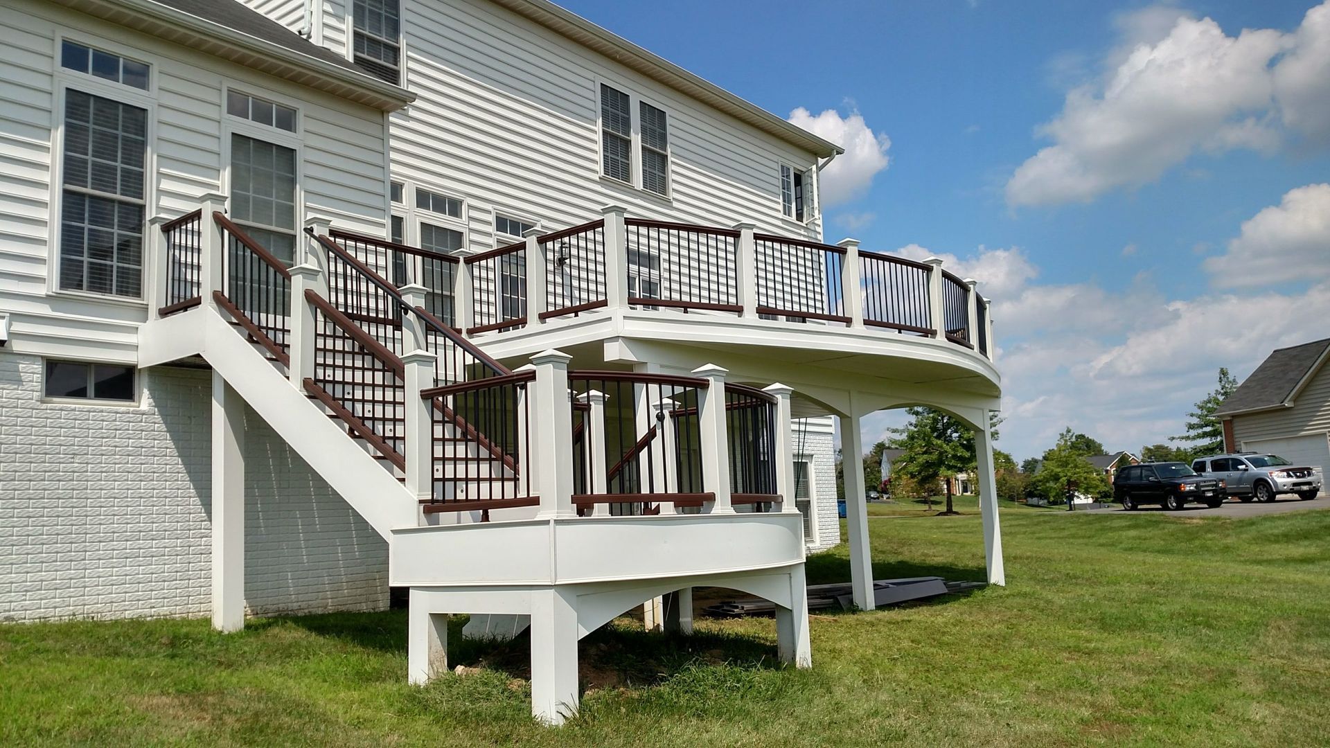 White house with curved deck and stairs in a sunny grassy yard under a blue sky