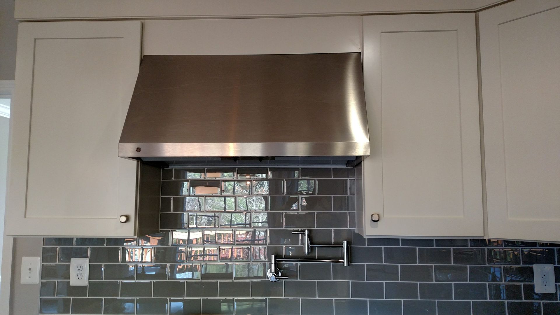 Kitchen backsplash with blue tile, white cabinets, and a stainless steel range hood above the stove area