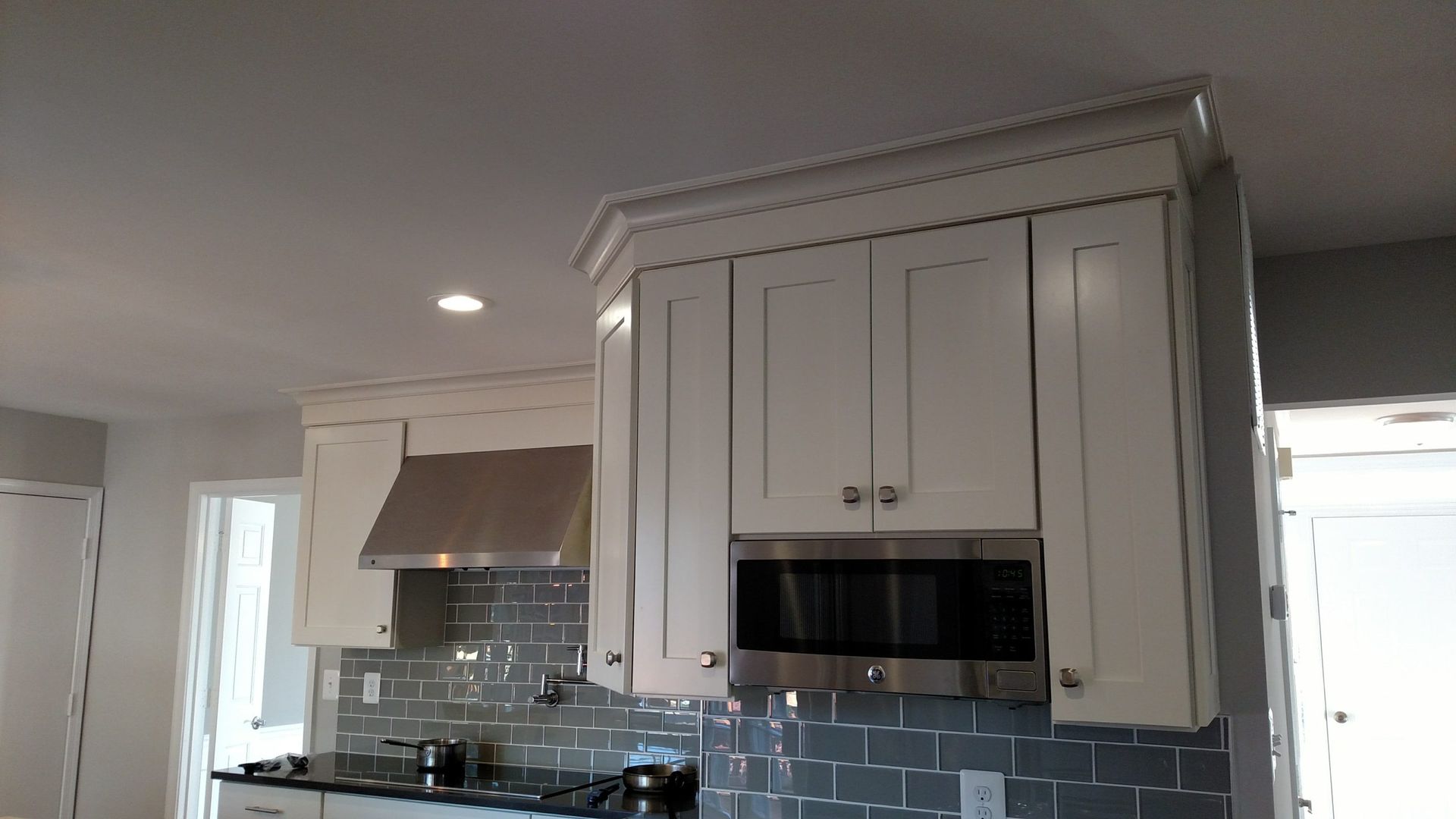 Modern kitchen with white cabinets, gray tile backsplash, stainless range hood, and built-in microwave.
