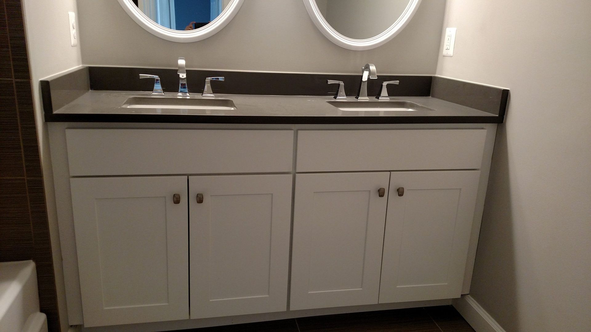Bathroom vanity with double sinks, dark countertop, and round mirrors above white cabinets.