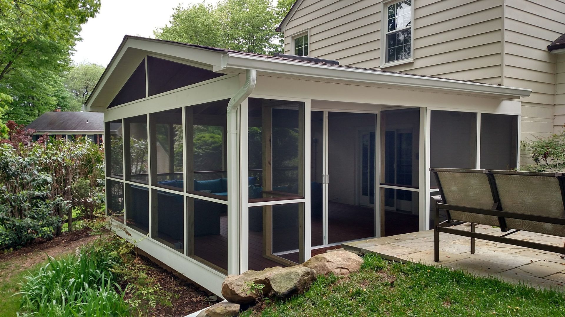 Screened porch attached to a beige house, with patio chairs and a grassy backyard.