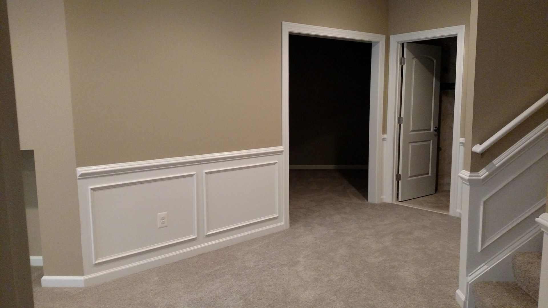 Empty carpeted hallway with beige walls, white trim, and an open doorway leading into a dark room.