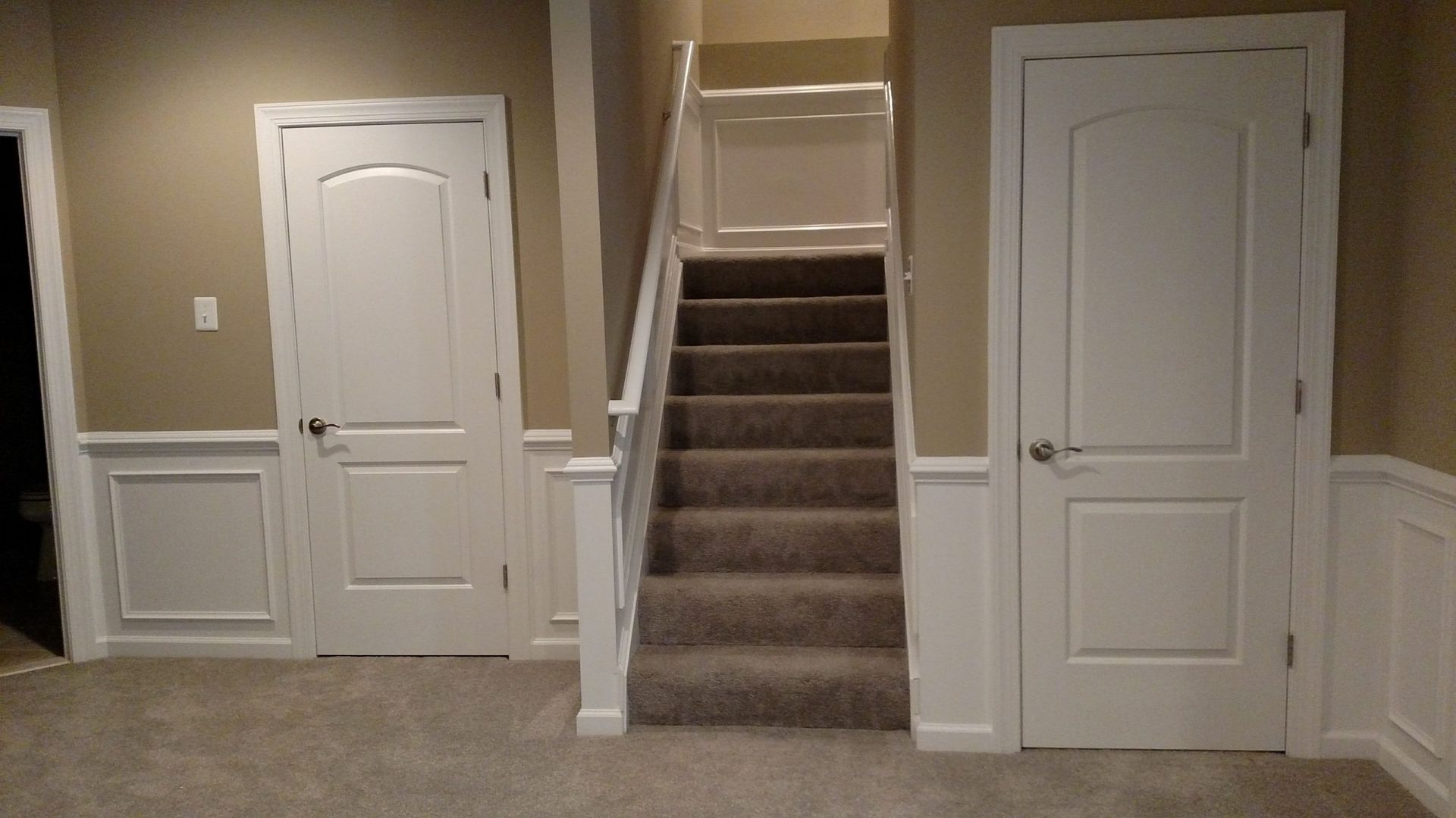 Basement hallway with carpeted stairs centered between two white doors and beige walls.
