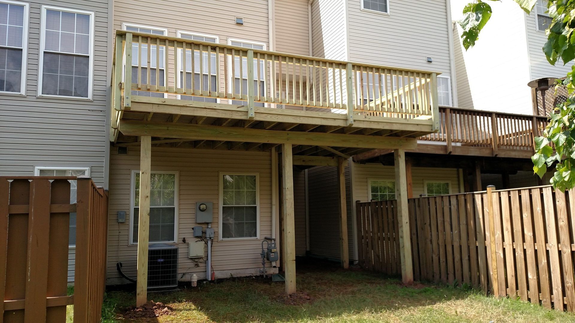 Backyard view of a house with an elevated wooden deck and stairs over a grassy yard fenced on both sides