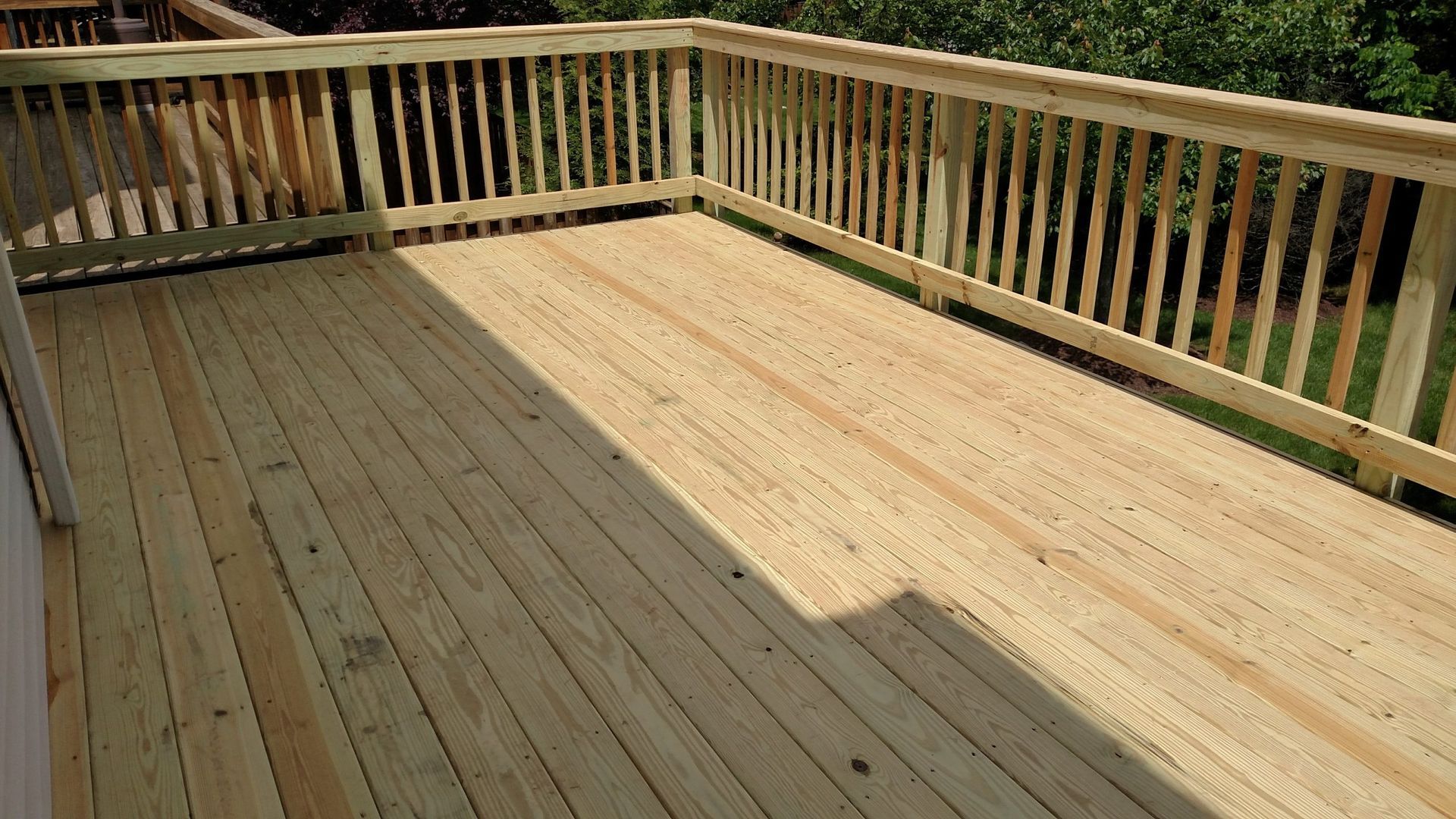 Wooden deck with railings, partly sunlit and partly shaded, viewed from above.