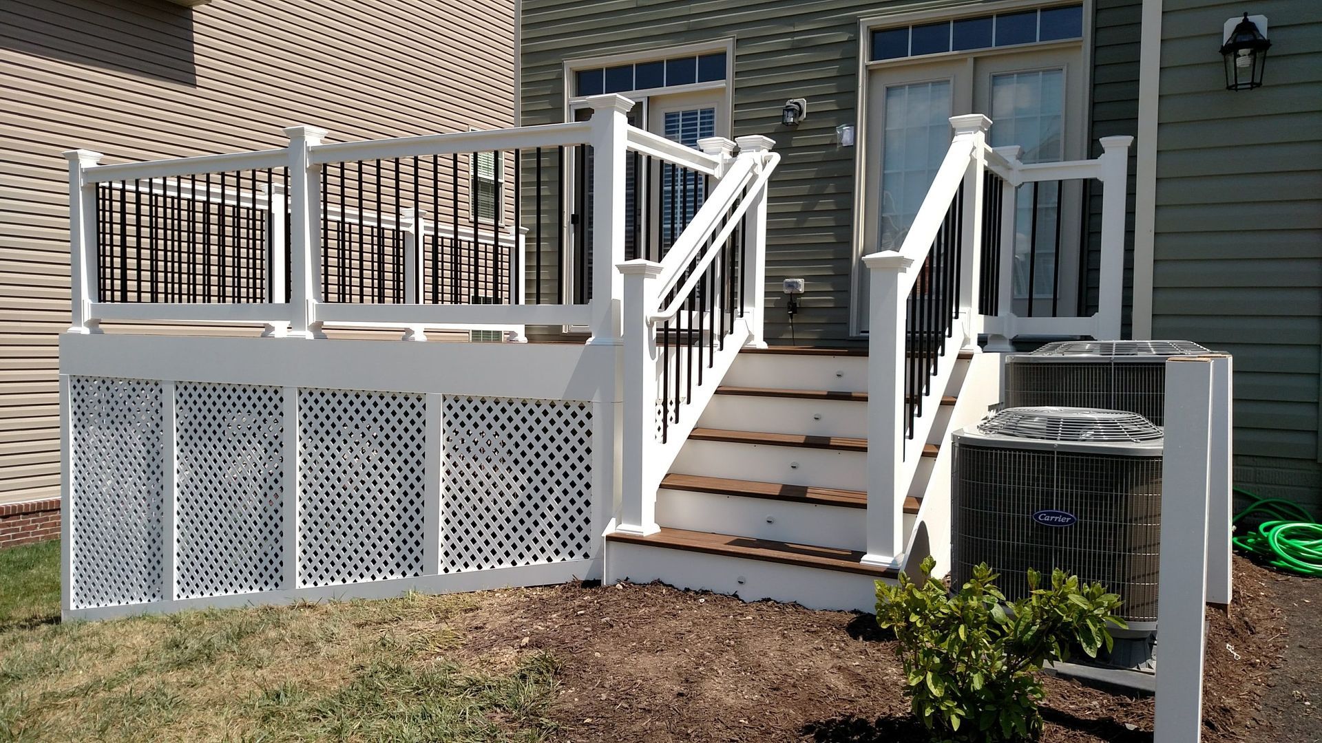 White accessible front deck with stairs, ramp, and lattice skirting on a brick house exterior