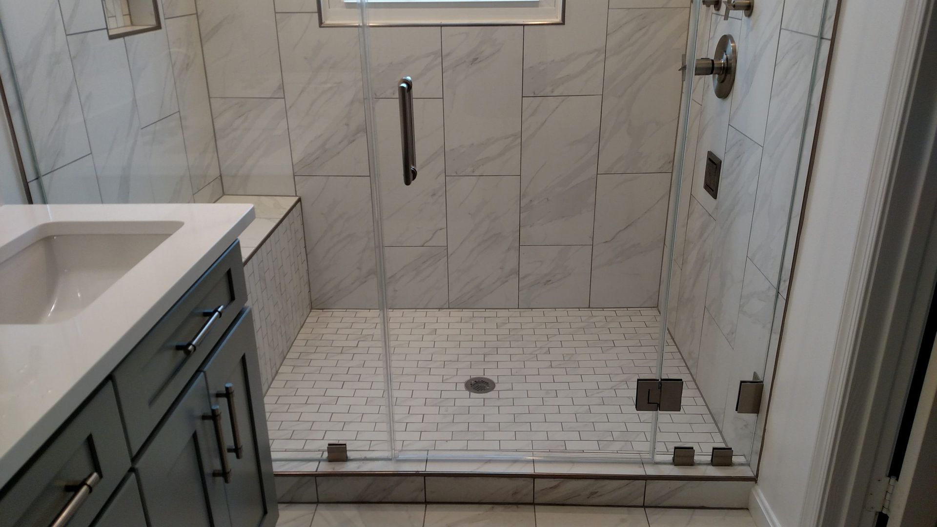 Small tiled walk-in shower with a low curb, grab bars, and a built-in bench in a bathroom