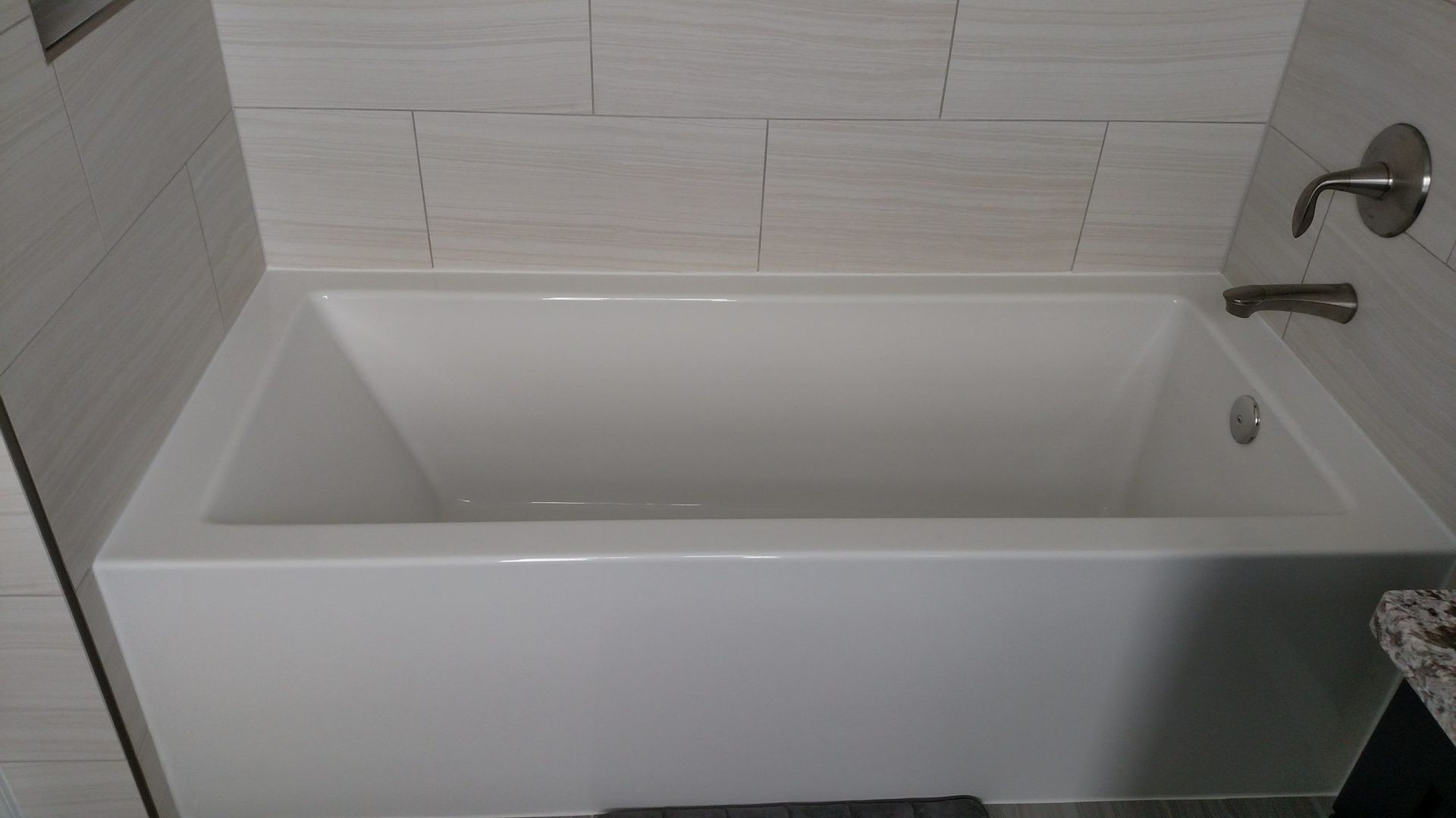 Modern white bathtub with chrome faucet and tiled bathroom wall.