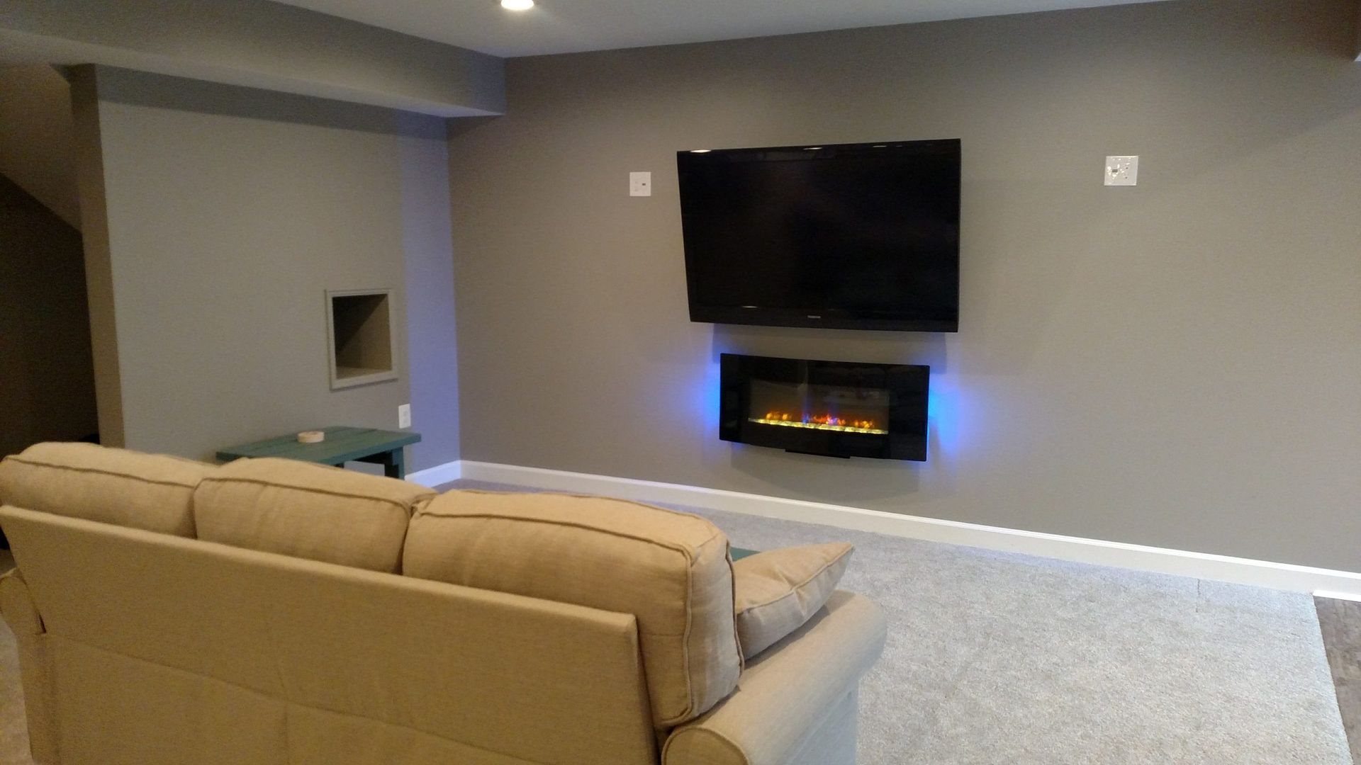 Living room with beige sectional, wall-mounted TV, and electric fireplace on a gray wall.