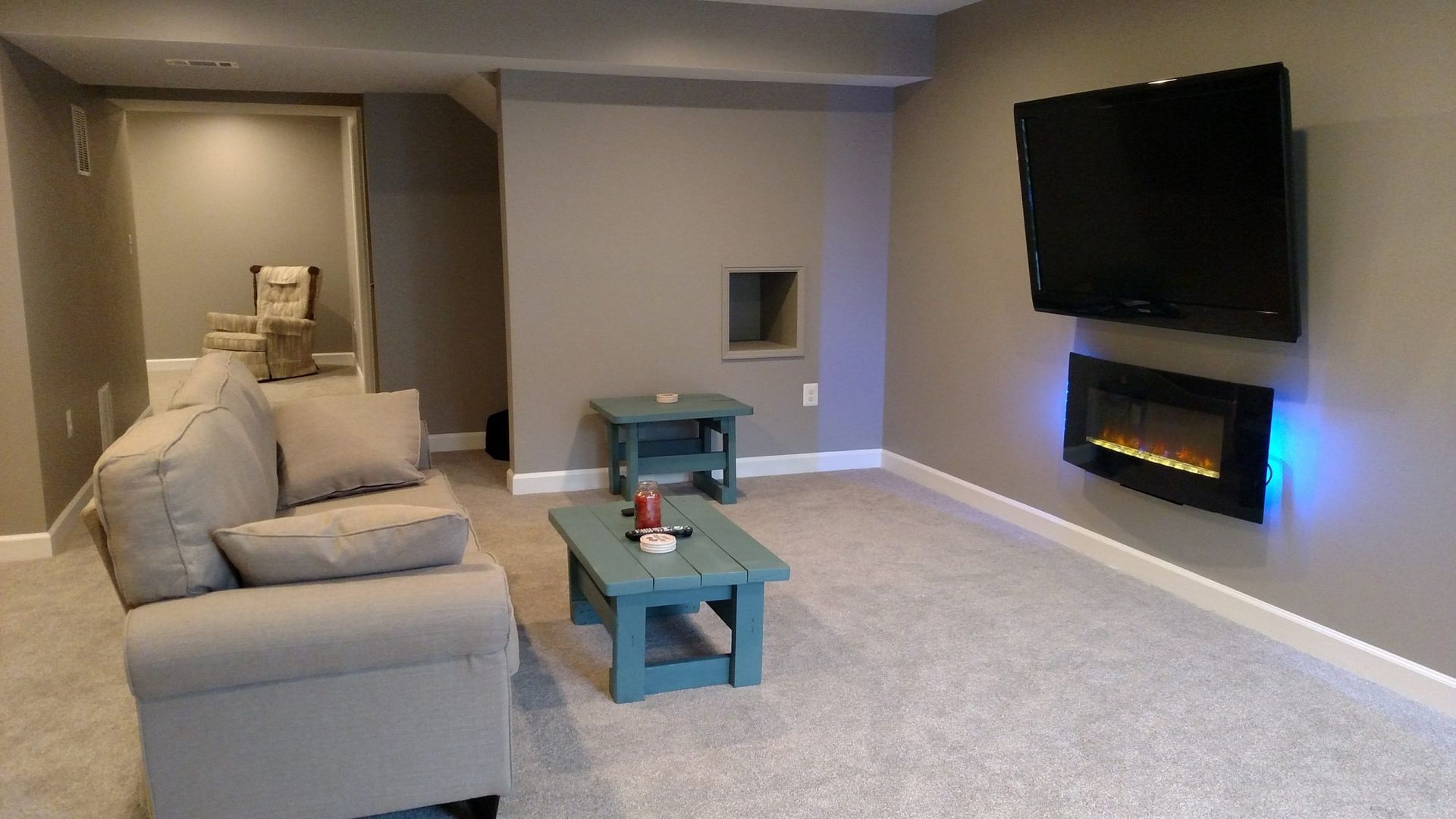 Modern living room with beige sectional, teal tables, wall-mounted TV, and electric fireplace.