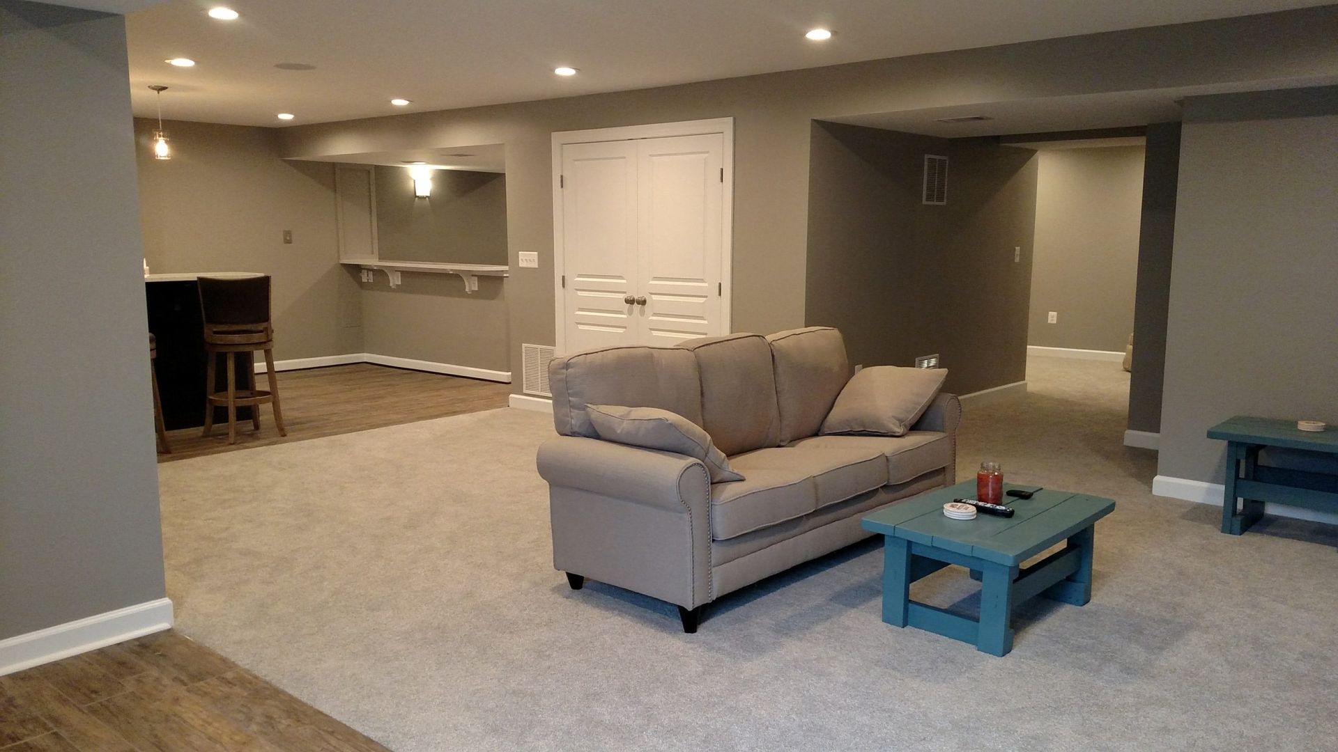Finished basement living room with beige carpet, gray sofa, and blue coffee tables.