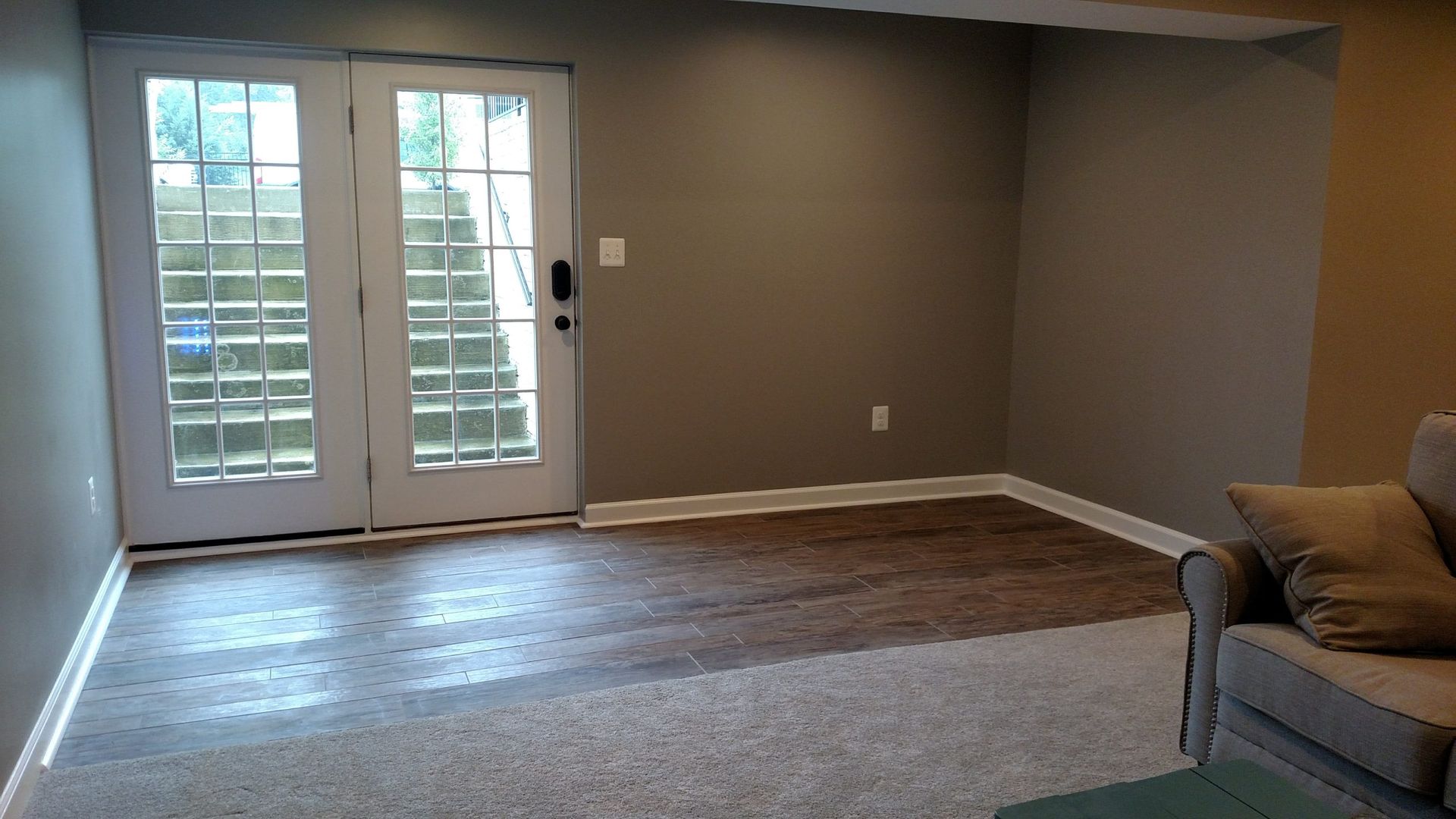 Empty living room with hardwood floor, beige walls, French doors, and a partial sofa on the right.