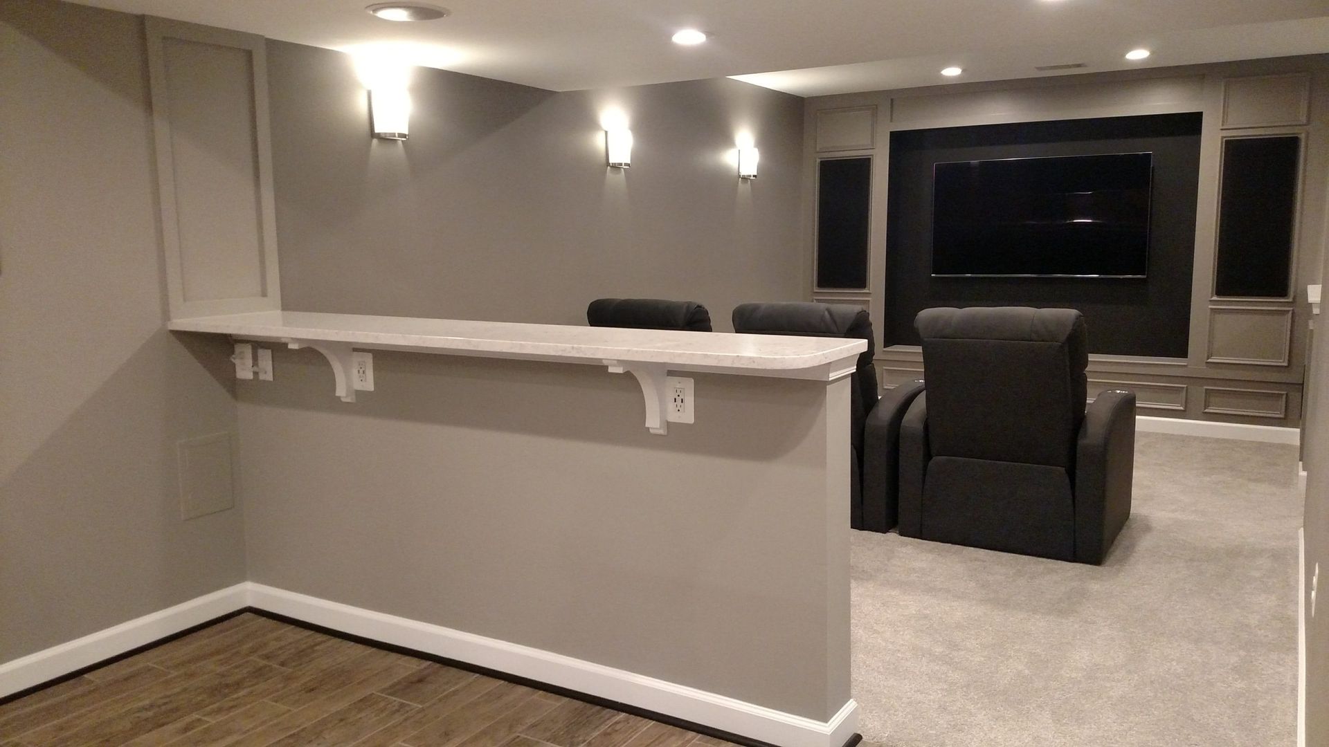 Basement home theater with gray walls, bar ledge, black recliner, and large TV screen