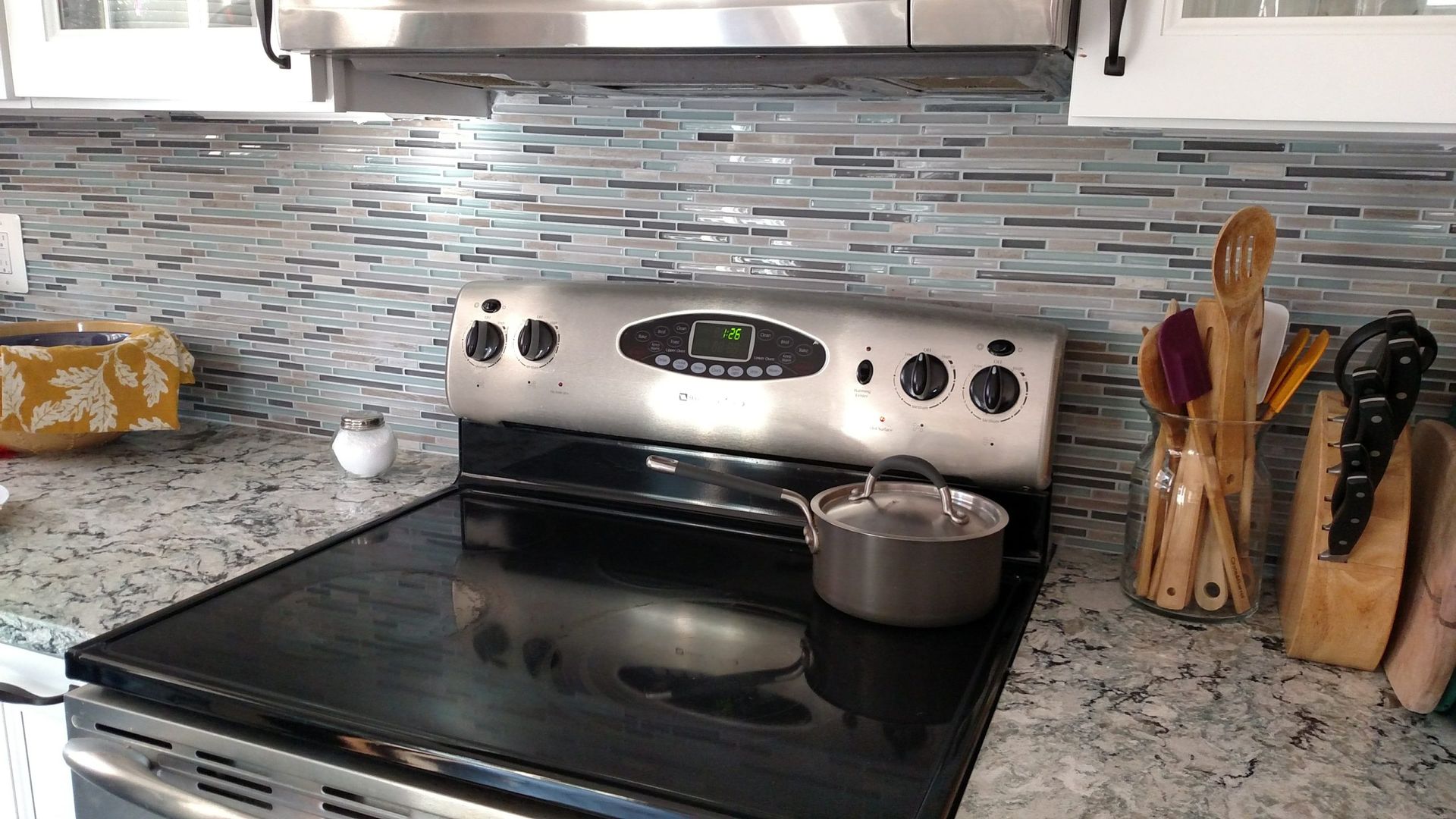 Kitchen stove with a pot on the front burner, stainless steel backsplash, and utensil holder on the counter.