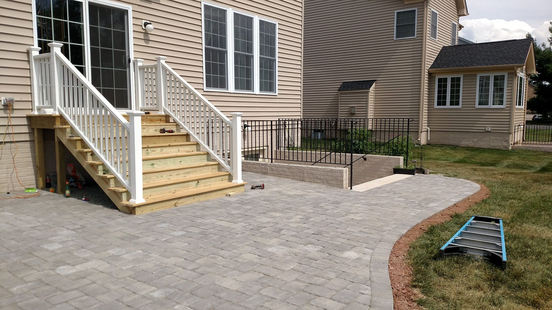 Backyard patio with stone pavers, wooden stairs, and a fenced garden area beside a house