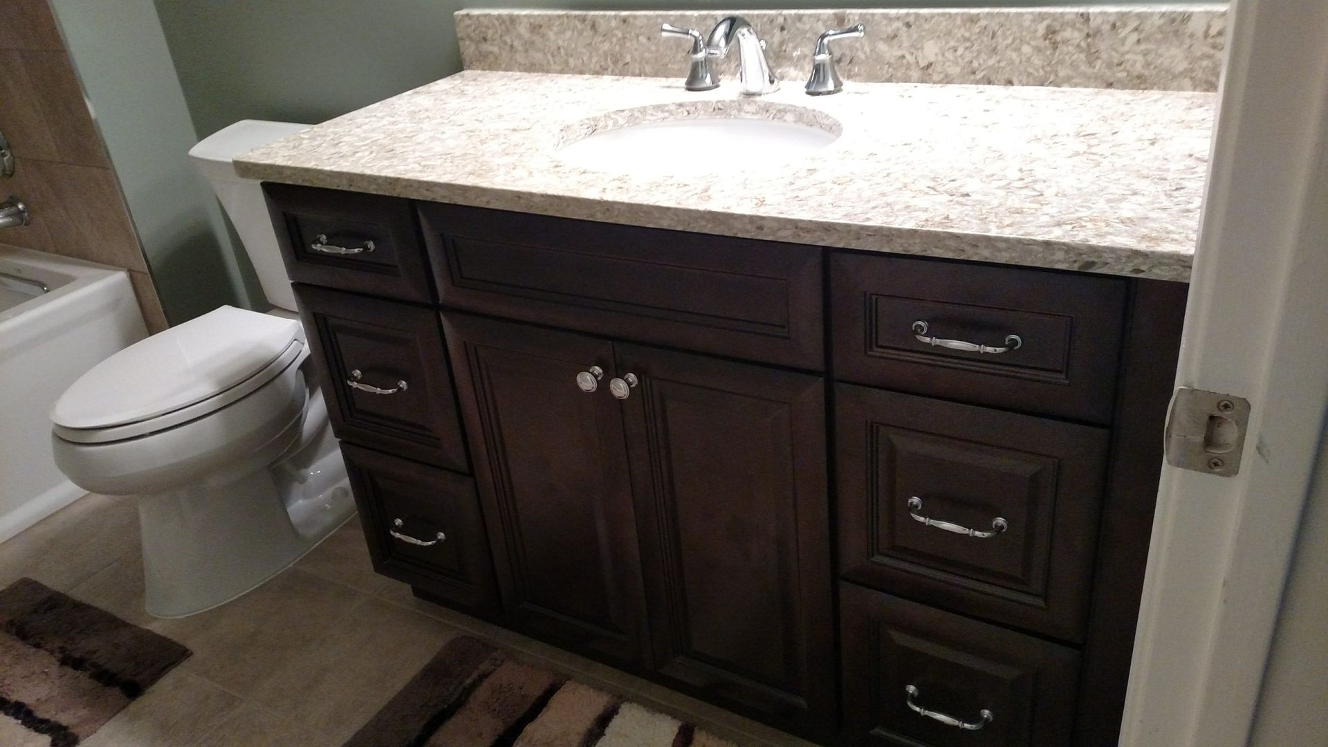 Bathroom vanity with dark wood cabinets, light granite countertop, sink, mirror, and white toilet.